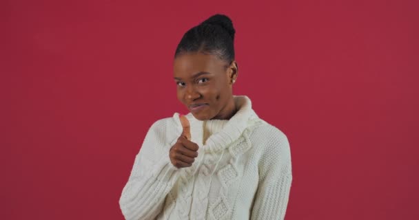 Portret van Afro Amerikaanse vrouw model staat in studio op rode achtergrond draagt witte trui meisje met donkere huid toont hand als maakt gebaar van goedkeuring brengt vinger omhoog demonstreren succes overwinning — Stockvideo