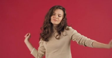 Kırmızı arka planda dans eden uzun saçlı, çılgın, neşeli, parlak, başarılı genç kız kollarını ve vücudunu müziğe yönelterek gençlik güzelliğinin ve parti konseptinin keyfini çıkarıyor.