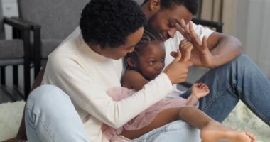 Başarılı ve sevgi dolu bir aile hafta sonu birlikte vakit geçirip yerde oturuyor, Afro-Amerikan genç yetişkin çift ve akıllı küçük kız çocuğu el ele tutuşuyor.