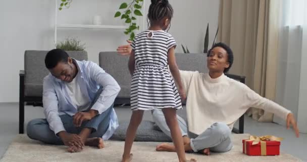 Τρεις Αφροαμερικανοί γονείς για την κόρη τους μαζί στο σαλόνι, η μαμά δίνει στην κορούλα κόκκινο κουτί δώρου για τις εορταστικές αγκαλιές των παιδιών γενεθλίων μητέρα, αγαπημένη εθνοτική οικογένεια γιορτάζει στο σπίτι — Αρχείο Βίντεο