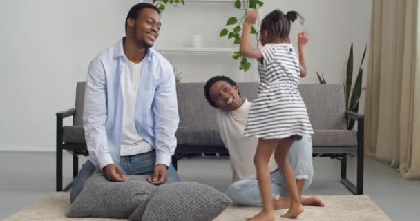 Ung afro amerikansk familj leker hemma sitter på golvet, tre människor föräldrar och söt liten flicka dotter tillbringa tid tillsammans på helgen skrattar hoppa dans kudde kamp kärlek koncept — Stockvideo