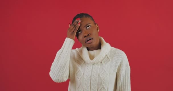 Retrato de estudio de una mujer afroamericana sosteniendo su cabeza sufriendo de dolor de cabeza tensión dolor de cabeza preocupaciones por problemas en el trabajo se encuentra aislado sobre fondo rojo, expresión triste de cara femenina — Vídeo de stock