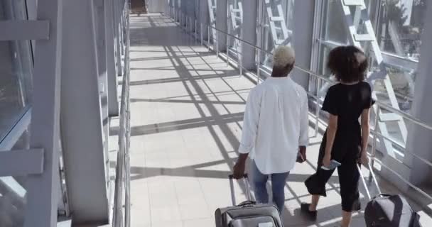 O casal afro-americano vai ao aeroporto aterrar com malas a falar. Dois estranhos adolescentes empresários colegas amigos movem-se ao longo do corredor do terminal depois de chegar no novo país — Vídeo de Stock