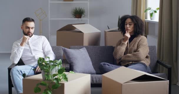 Межрасовые отношения афро-американская кудрявая женщина и кавказский мужчина грустная пара сидя на диване грустно из-за проблем с переездом ипотечного выселения из квартиры испытывает развод — стоковое видео