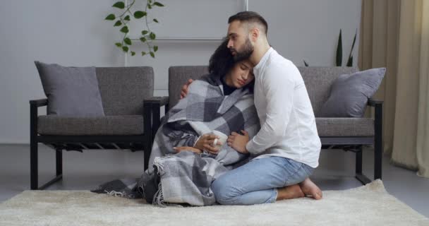 Loving caucasico uomo lenitivo triste sconvolto afro americano donna con bianco tazza di tè in mani avvolto in coperta scusarsi dopo interruzione lite indesiderata gravidanza, fidanzato abbraccio sostegno fidanzata — Video Stock