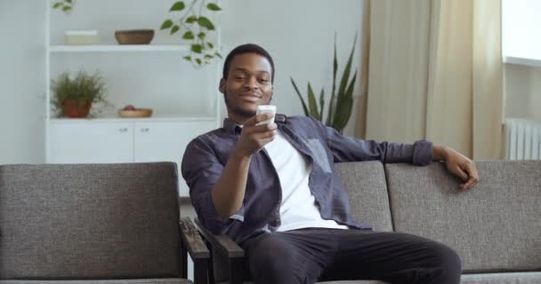 Afro-americano misto raça cara preto masculino estudante relaxante em casa sala de estar sofá assistindo tv online vídeo filmes mudando canais com controle remoto conceito para relaxar nos fins de semana no tempo livre — Vídeo de Stock
