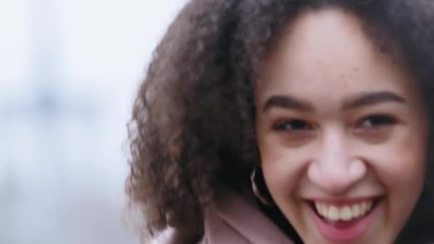 Portrait of afro american millennial girl with perfect dark skin makeup with curly hairstyle wearing scarf looking at camera outdoors laughing fully chuckles with joke, satisving expression — Stok Video