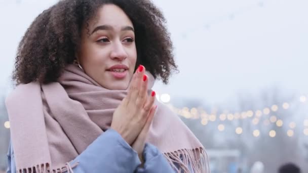 Portrét africké americké dívky pocit chladu trpí zmrazením tře si dlaně foukání teplý vzduch na rukou uniká zimní počasí s úsměvem vydechuje páru z úst stojí sám venku — Stock video