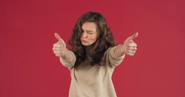 Portrait of young positive millennial caucasian girl teen stose on red studio background dancing moves to music showing thumbs up put like symbol support accepting symbol of exceased work — Stok Video