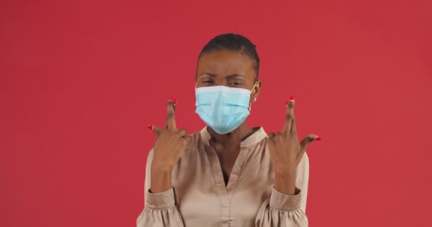 Portret van Afro-Amerikaanse etnische aardige meisje dragen veiligheid beschermende medische masker gekruiste vingers hoop op goede testresultaten voor negatieve covid test coronovirus maakt gebaar van hoop vraagt veel geluk — Stockvideo