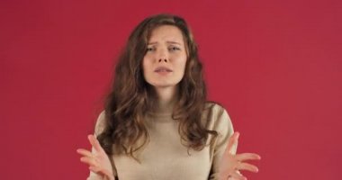 Kırmızı stüdyo arka planındaki portre beyaz kadın bin yıllık uzun saçlı genç kız öfkeyle el sallıyor olumsuz tutumlar, hoşnutsuzluk jestleri yapıyor.