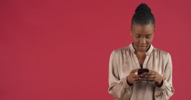 Neşeli Afrikalı Amerikalı genç bir kızın modern cep telefonuyla sohbet eden, iyi internet bağlantılarından hoşlanan, kırmızı duvarda izole bir şekilde bilgisayar mobil oyunu oynayan neşeli bir stüdyo fotoğrafı.