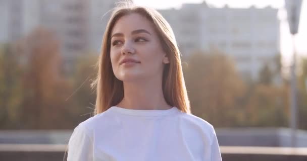 Street portrait of young blonde woman with long hair stands posing in front of camera outdoors straightens hairstyle. Teenager student girl enjoying sunny weather youth and life walking around city — Stock Video