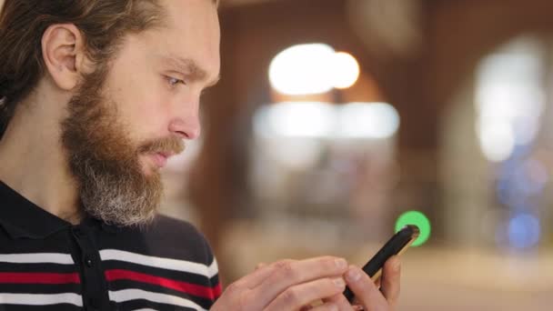 Πλάγια άποψη της γενειοφόρος νεαρός ενήλικας επιχειρηματίας καταναλωτή χρησιμοποιώντας το κινητό τηλέφωνο για να αγοράσει σε απευθείας σύνδεση επιλέγει προϊόν σερφάρισμα στο διαδίκτυο γραπτών μηνυμάτων σε κοινωνικά δίκτυα που εργάζονται κοιτάζοντας οθόνη smartphone, close-up — Αρχείο Βίντεο