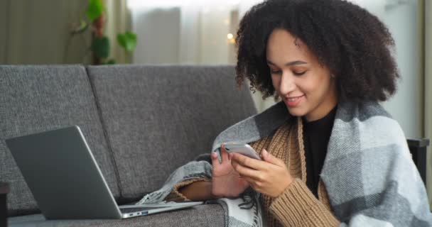 Sorrindo positivo motivado estudante mulher de negócios adolescente sentado em casa na sala de estar no sofá usa smartphone móvel e laptop para o trabalho estudo remoto mensagens de texto com amigos em redes sociais — Vídeo de Stock