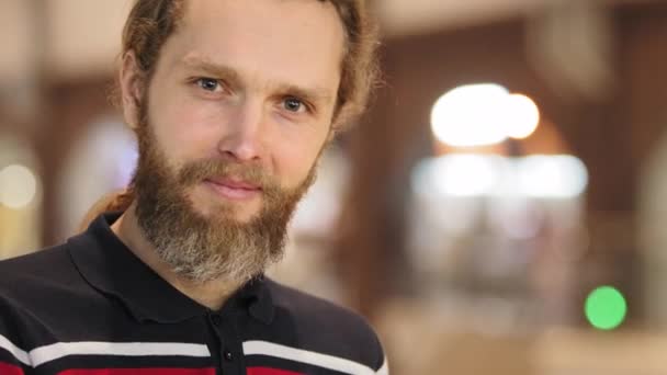 Close-up of emotional attractive man with beard and long hair wears casual clothes looking at camera grimaces male face squints his eyes points with finger direction or road makes hand appeal gesture — Stock Video