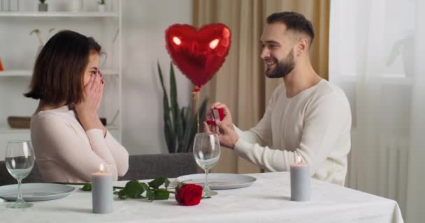 Pareja cenando en casa celebrando el aniversario del día de San Valentín, cariñoso esposo caucásico da regalo con anillo de diamante a su amada mujer, novio hace propuesta de matrimonio, cásate conmigo — Vídeos de Stock