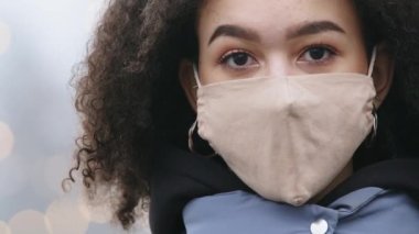 Maskeli kadın yüzü, halka açık bir yerde duran ciddi esmer ciltli kıvırcık kadın koruyucu bir maske takıyor karantinada kentsel arka planda gelişigüzel poz vererek yürüyor.