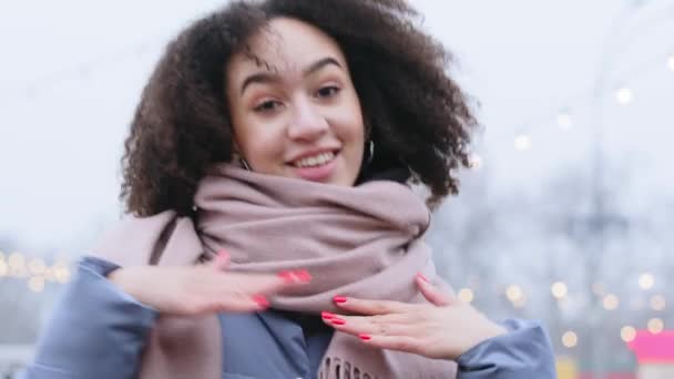 Portret szczęśliwej uczennicy nastolatki pani ciemnoskóry wesoły dziewczyna ze stylowymi kręconymi afro włosy nosi modny szalik stoi sam na zewnątrz w zimie tańce porusza jej ręce aktywnie — Wideo stockowe