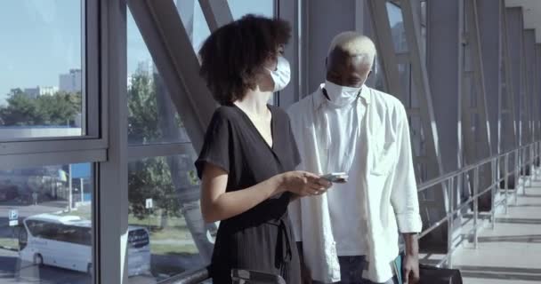 아 프로 아메리칸 커플은 신혼 여행을 위해 코로나 바이러스에 맞서 의료용 마스크를 착용하고 공항에서 비행기 표를 들고 서 있으며 함께 시간을 보낸다. — 비디오