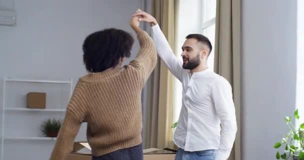 Heureux jeune couple mixte célébrant le déménagement à la maison développement du changement dans la vie familiale nouvelle étape de la relation dansant ensemble dans le salon entouré de boîtes d'emballage rire se réjouissant — Video