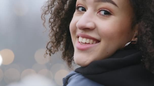 Close-up profiel van vrouwelijke gezicht van Afrikaanse nationaliteit zwarte krullende dame weg te kijken in de camera glimlachend met witte tanden dromen buiten in de stad ademen koude winterlucht, model portret — Stockvideo
