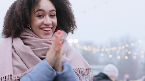 Glimlachend Afro-Amerikaans meisje 20-30 jaar oud millennial vrouw model staat op straat in drukke plaats in de open lucht bevriest van lage temperatuur slagen op de palm wrijft haar handen warm te houden in de winter — Stockvideo