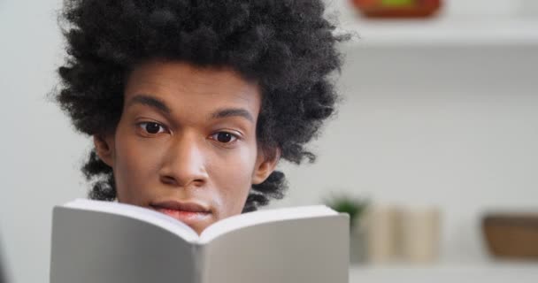 Close-up dark skined male face afro american young ethnic guy student teenager hides behind book reads novel to end feels shock sadness upset from unexpected negative final expresses unhappy emotions — Stock Video