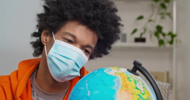 Lonely african american black man traveler looking at globe with sad wants to travel suffers from lock down and isolation in his home with medical mask on face, foreign student misses his country — Stock Video