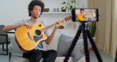 Erkek vlog teather afro sanatçısı müzik gösterisi yapıyor. Evde oturarak internet üzerinden gitar çalmayı öğretiyor. Cep telefonuyla çekim yapan siyahi adam İnternet günlüğü için şarkı söylüyor