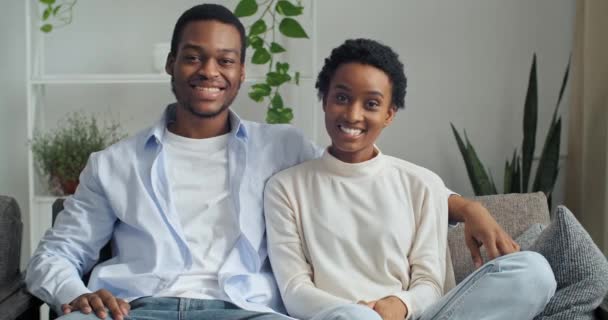 Casamento feliz casal étnico sentado no sofá em casa sala de estar. Retrato afro-americano esposa e marido acenando as mãos olhando para câmera sorrindo falando saudação falando em vídeo se comunicar online — Vídeo de Stock