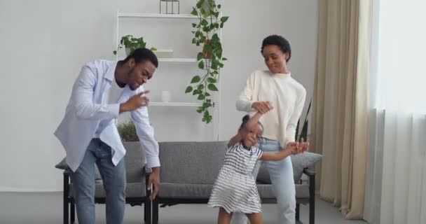 Tre personer afro amerikanska familj unga par dans med sin älskade förskola flicka dotter tillbringa tid tillsammans hemma undervisa dans flytta till musik hoppa ha kul, semester koncept — Stockvideo
