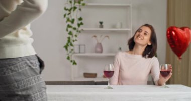Arkasından erkek erkeğe flört eden, arkası dönük kırmızı gül saklayan sevgili kız arkadaşı, sevgililer gününde kadınları tebrik etmek için masanın yanında duruyor.