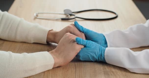 Κοντινό πλάνο των ιατρών χέρια σε μπλε γάντια λατέξ κατέχουν ανδρικές παλάμες του καυκάσιου άνδρα βρίσκονται στο τραπέζι κοντά στηθοσκόπιο, σύμβολο της υποστήριξης κατά τη διάρκεια της θεραπείας, ιατρικός επαγγελματίας ηρεμεί τον ασθενή κρατώντας τα όπλα — Αρχείο Βίντεο