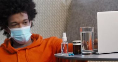 Afro-Amerikalı genç adam portresi evde dinlenen tıbbi koruyucu maske takıyor. Virüs belirtileri gösteriyor. Haplar uzaktan dizüstü bilgisayara bakıp internetten film izliyor.