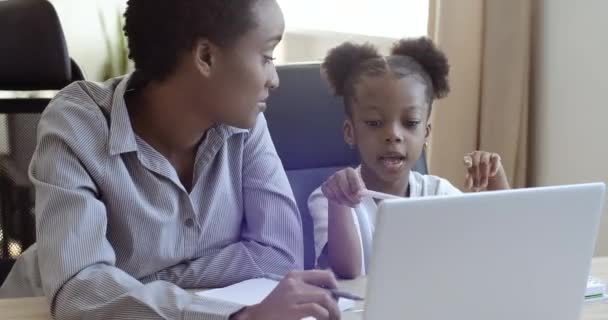 Afrikaanse zwarte vrouw moeder helpen schattig geliefde dochter schoolmeisje met huiswerk zitten samen op laptop studie online in netwerk schrijven op papier notities maken in notebook, home onderwijs leren concept — Stockvideo