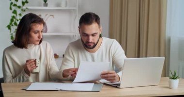 Bin yıllık Kafkasyalı çift evde ev ödevlerini hesaplarken dizüstü bilgisayarla internet üzerinden ödeme yaparken mutlu bir aile babası, elinde çay bardağıyla bir fincan çay tutarken bütçesini planlarken tamam jestini gösteriyor.