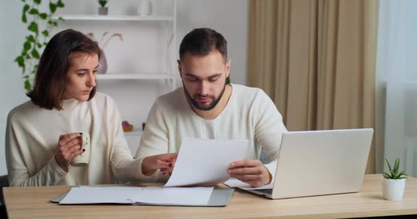 Fokuserad tusenårig kaukasiska par beräkna inhemska pappersräkningar hemma med hjälp av bärbar dator betala online i nätet, lycklig familj man planerar budget med kvinna som håller kopp te visar ok okej gest — Stockvideo