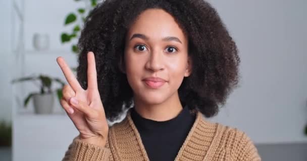 Close-up front portrait of african american positive teen girl posing indoor shows two fingers v letter making peace gesture counts numbers dancing brings his hands to his eyes face moves coquettishly — Vídeo de Stock