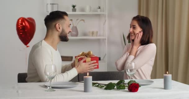 사랑하는 코카서스 남자 친구는 사랑하는 아내에게 생일 선물로 빨간색 선물 상자를 주는데, 생일 축하 선물 부부는 친밀감과 애정의 상징으로 포옹 한다 — 비디오