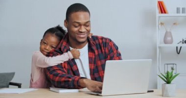 Afro-Amerikan iş adamı serbest çalışan pazarlamacı baba ana ofiste dizüstü bilgisayarla çalışıyor sevgi dolu kızı kucaklıyor baba ilgi istiyor.