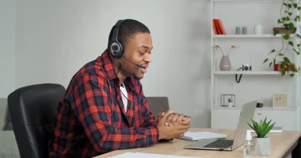 Afro american student guy in casual shirt in cage wears headphones speaks into laptop webcam with teacher answers exam, freelance business man conducts interview negotiation online video conference — Stock Video