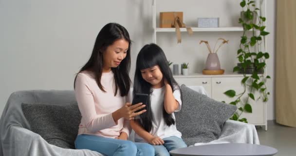 Étnica familia asiática mamá con hija viendo película de dibujos animados divertido vídeo riendo usando el teléfono móvil tomar selfie en cámara de gadget para redes sociales, madre muestra niño máscaras aplicación de fotos — Vídeo de stock