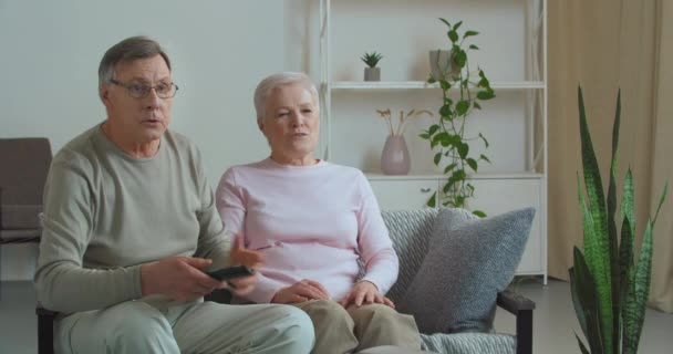 Casal de idosos caucasianos aposentados passando fim de semana em casa assistindo jogo na TV torcendo por sua equipe favorita construindo para perder pontuação ruim velho irritado joga controle remoto fora de descontentamento — Vídeo de Stock