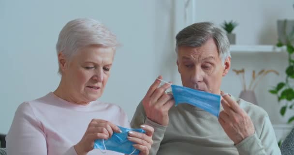 Pareja de ancianos caucásicos de pelo gris hombre y mujer de edad madura familia sentados juntos en casa aislado celebración poner en máscaras de protección médica discutir pandemia de virus pandémico, concepto de bloqueo — Vídeo de stock