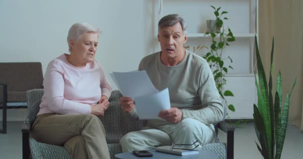 Pareja de ancianos se sienta en casa en los papeles de espera sofá recibir documentos carta con malas noticias, enojado anciano molesto discute con la esposa madura sobre facturas préstamo preocupado por problemas con los gastos financieros — Vídeo de stock