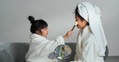 Spa banyosundan sonra bornoz giyen aile, Asya 'lı anne kafasına havlu takıyor Koreli kız kızla oturuyor, çocuk anne için makyaj yapıyor cilt okşayan kadın yanakları yüzüne allık sürüyor.