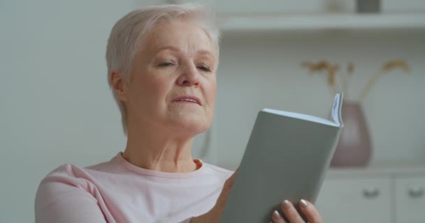 Oude blanke vrouw grijs harige oudere volwassen dame zitten thuis lezen boek weigert literatuur voor elektronische toestel telefoon kijkt naar smartphone scherm straightens haar haar, technologie concept — Stockvideo