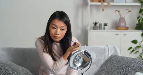 Confiado tranquilo centrado asiático joven mujer sosteniendo rímel aplicar en las pestañas prepararse para la fecha preparándose por la mañana, chica étnica haciendo maquillaje poner cosméticos en la cara mirando en espejo reflexión — Vídeos de Stock