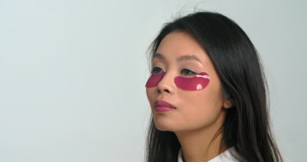 Gros plan belle jeune femme brune coréenne asiatique peau lisse et saine appliquant sous les yeux des patchs roses soin cosmétique naturel, portrait de la fille ethnique chinoise se débarrasse des rides, concept de jeunesse — Video